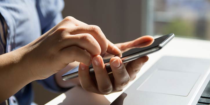 Someone using their mobile phone with a laptop in front of them